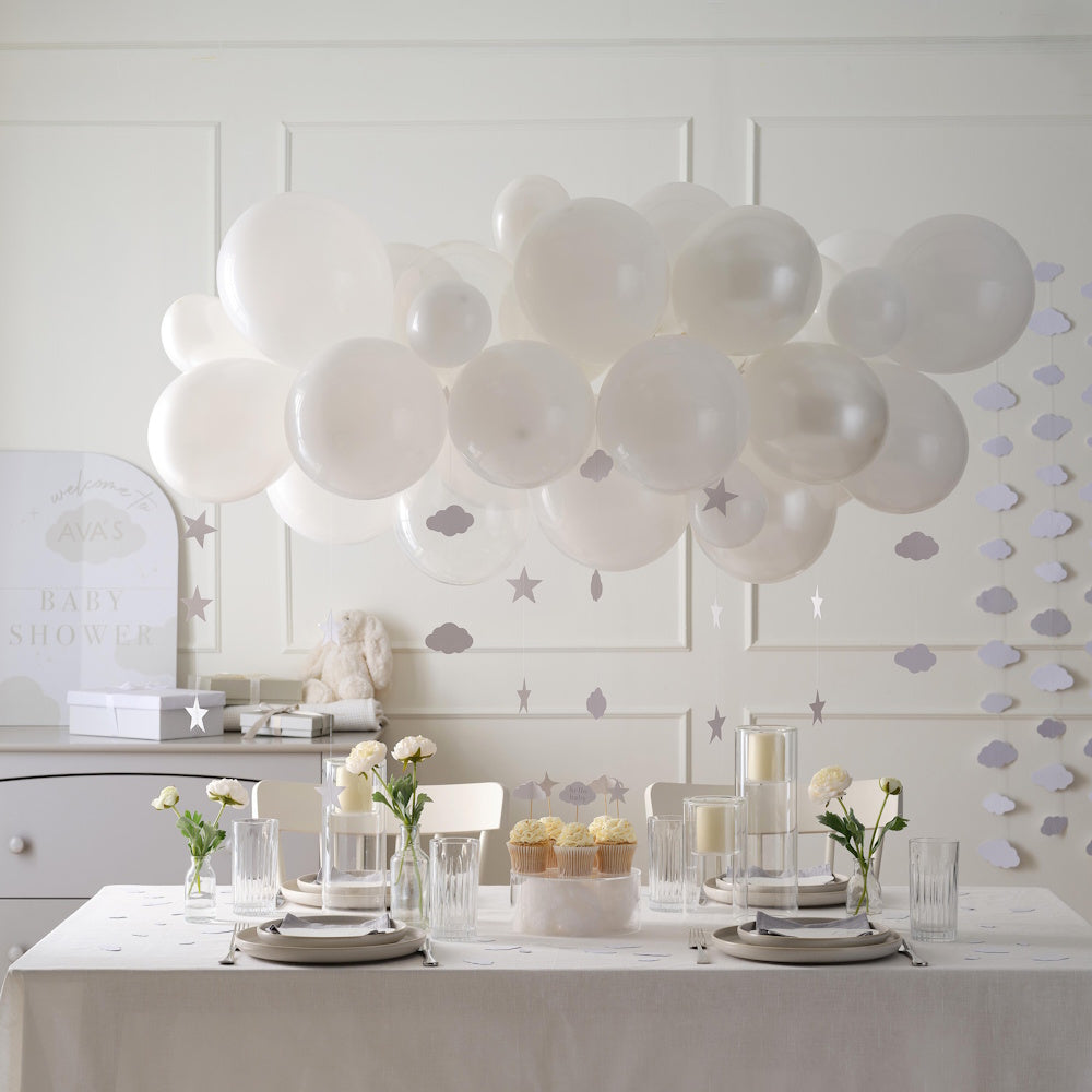 White balloons and decor in a room with a table set for a Baby Shower.